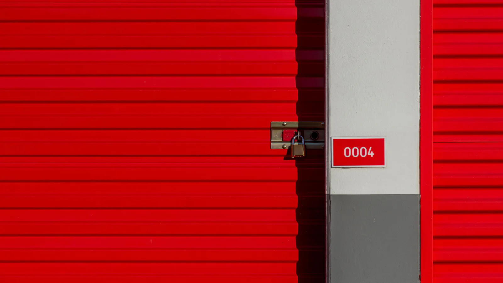 Puerta de unidad de almacenamiento roja con candado y número, representando boxes individuales de trastero | ZonaFranquicia