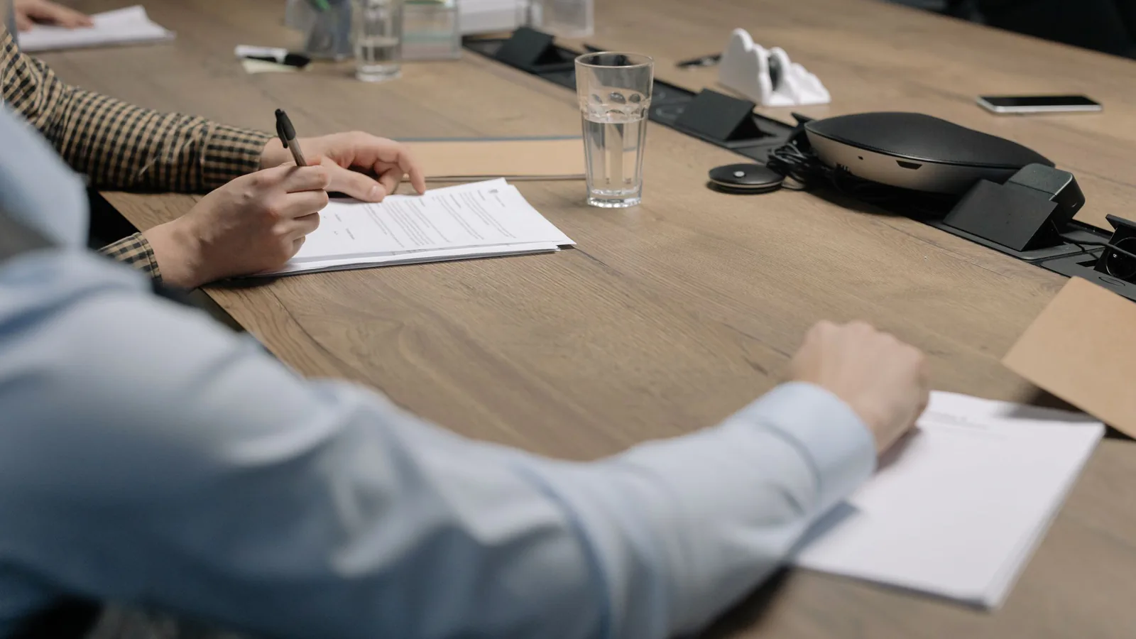 Cómo salir de una franquicia antes de tiempo sin arruinarte | ZonaFranquicia Dos profesionales firman documentos en una mesa de reuniones durante una negociación comercial | ZonaFranquicia