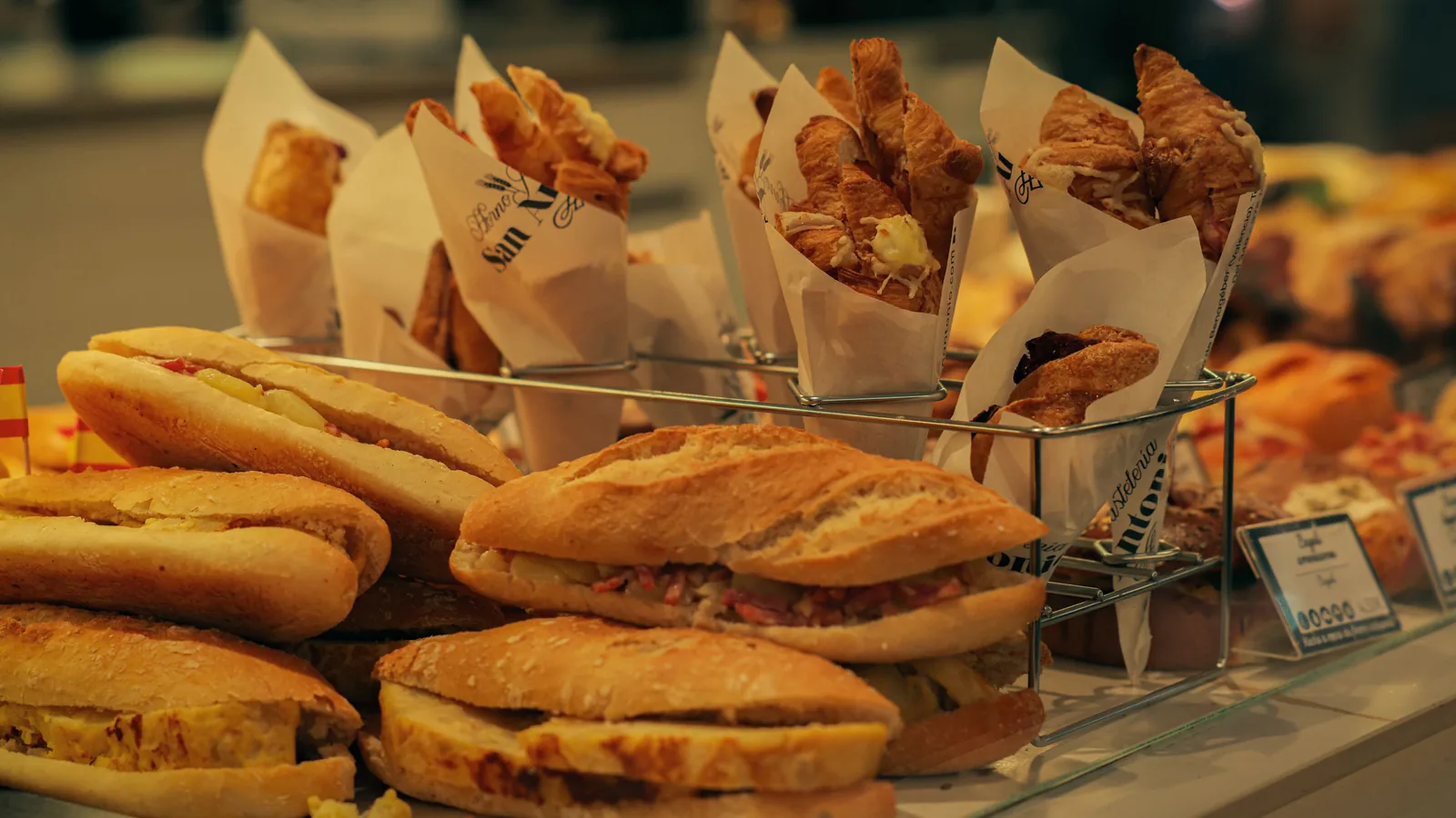 Compà, la franquicia de focaccia italiana, acelera en Barcelona y ya mira a Madrid y Valencia | ZonaFranquicia Escaparate de panadería con pasteles frescos y sándwiches variados expuestos, ambiente de comercio español | ZonaFranquicia
