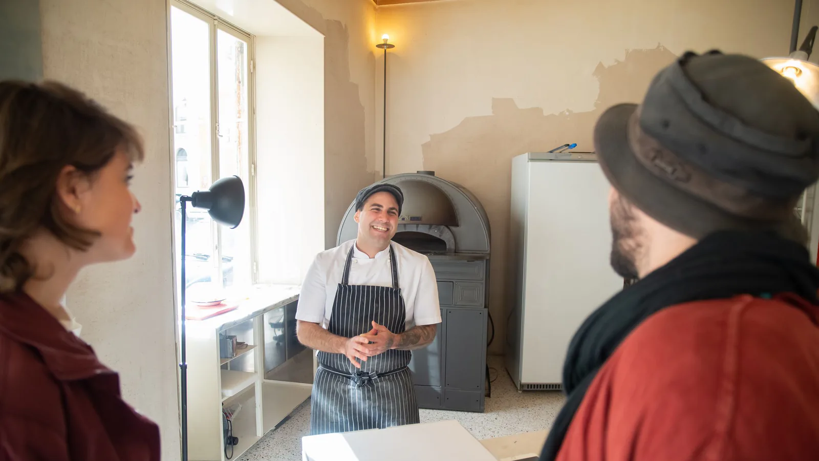Ditaly desembarca en Cádiz: la pizza al horno del grupo La Mafia acelera su expansión en franquicia | ZonaFranquicia Chef sonriente interactúa con pareja de clientes en acogedora pizzería, atmósfera acogedora | ZonaFranquicia
