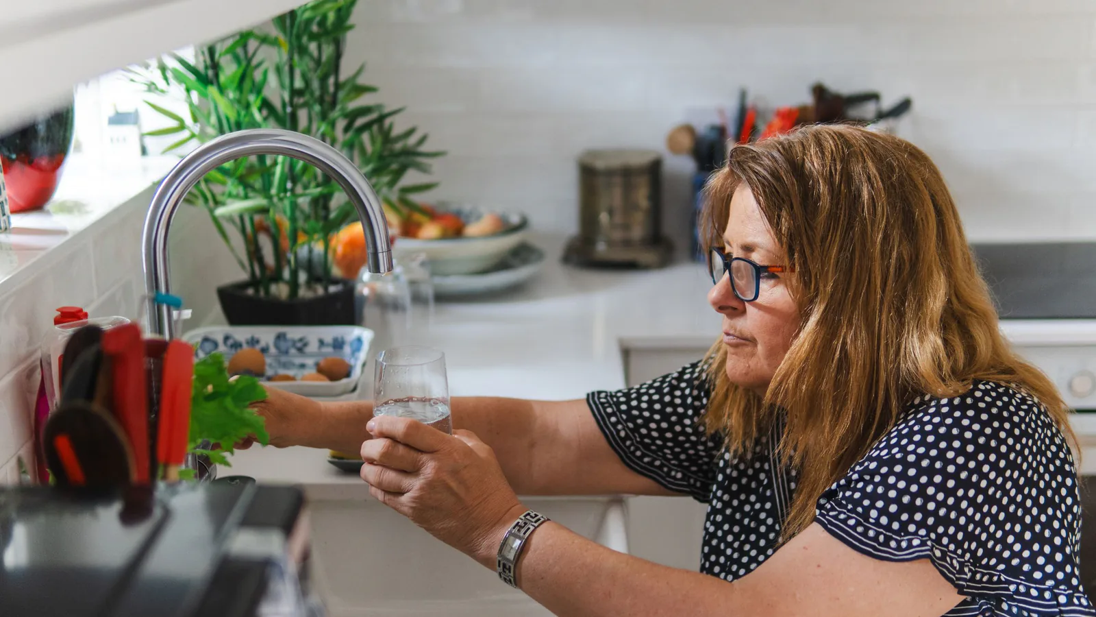 Doctor Agua estrena su primera tienda y se abre a franquiciados en el nicho del bienestar | ZonaFranquicia Mujer en cocina moderna sosteniendo vaso de agua filtrada junto a dispensador de agua | ZonaFranquicia