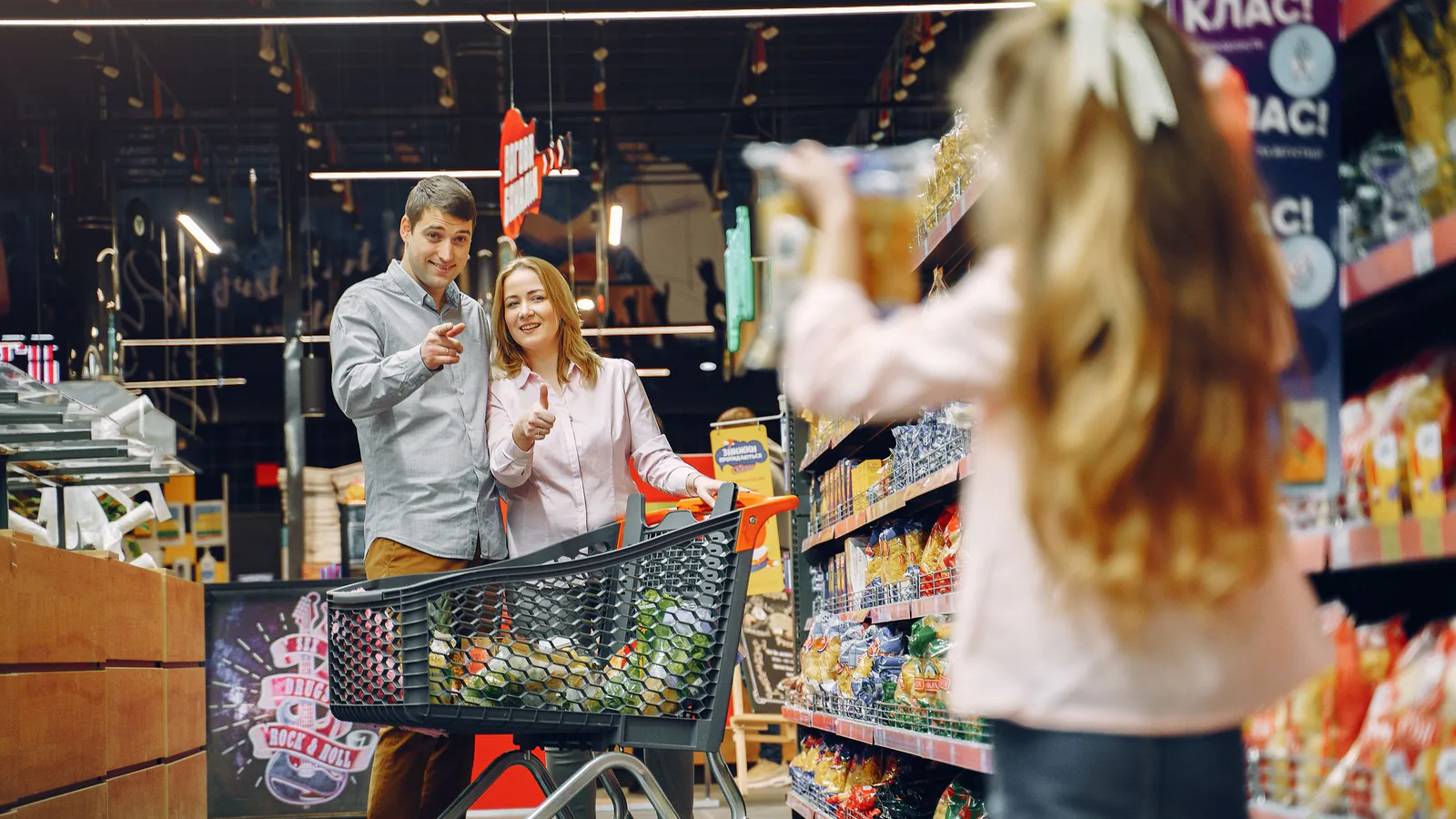 Familia feliz comprando en pasillo de supermercado, con niña sosteniendo caja de productos | ZonaFranquicia