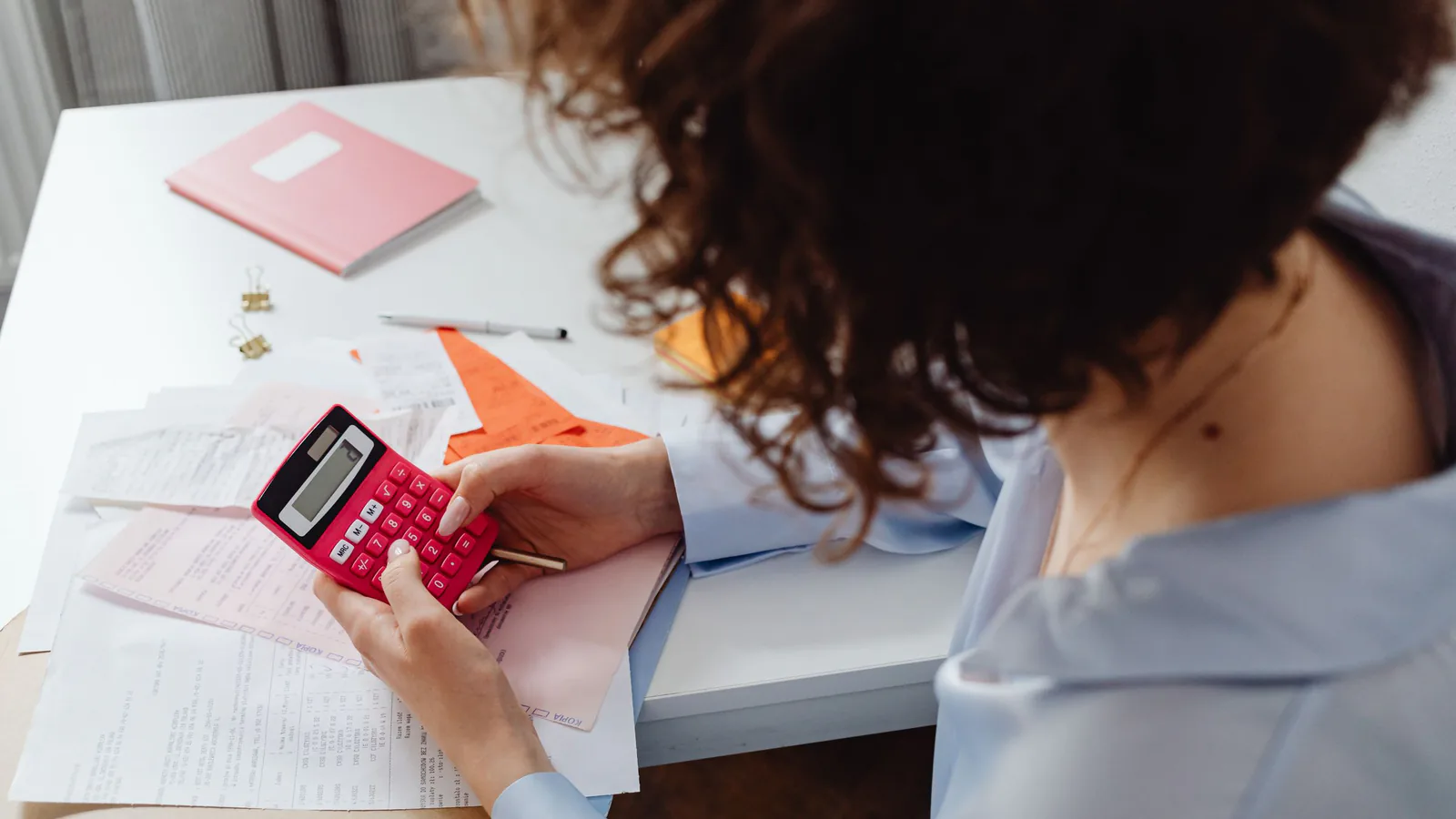 Mujer calculando gastos con documentos y calculadora en su escritorio de trabajo | ZonaFranquicia