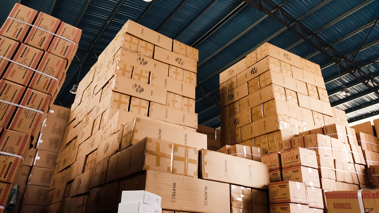 Franquicia con stock: evita el sobreestock que arruina | ZonaFranquicia Pilas de cajas de cartón organizadas en estanterías metálicas de un almacén industrial | ZonaFranquicia