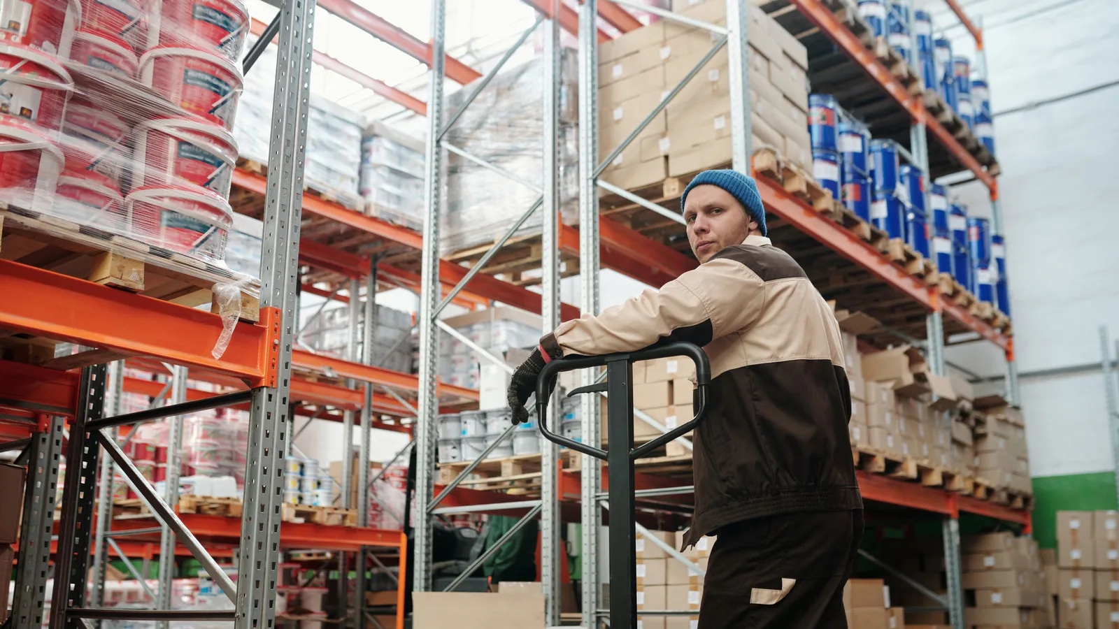 Franquicia de distribución: ganar dinero sin tienda ni empleados | ZonaFranquicia Trabajador de almacén operando una transpaleta entre cajas apiladas y estanterías metálicas | ZonaFranquicia