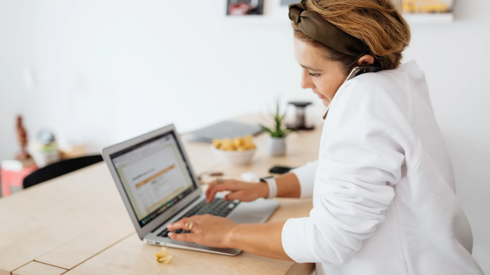 Franquicia online vs. física: cuál es más rentable en 2026 | ZonaFranquicia Mujer emprendedora multitarea con laptop y teléfono en escritorio moderno de casa | ZonaFranquicia