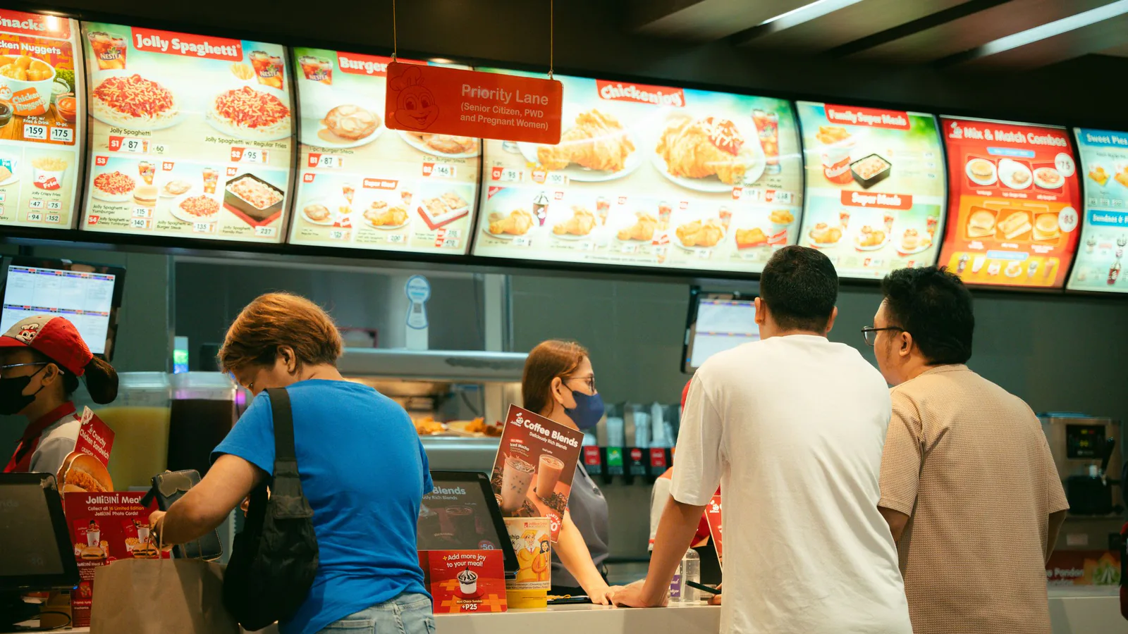 Frisby concede sus dos primeras franquicias en España: estas son las condiciones para invertir | ZonaFranquicia Cliente realizando su pedido en el mostrador de un restaurante de comida rápida con ambiente activo | ZonaFranquicia