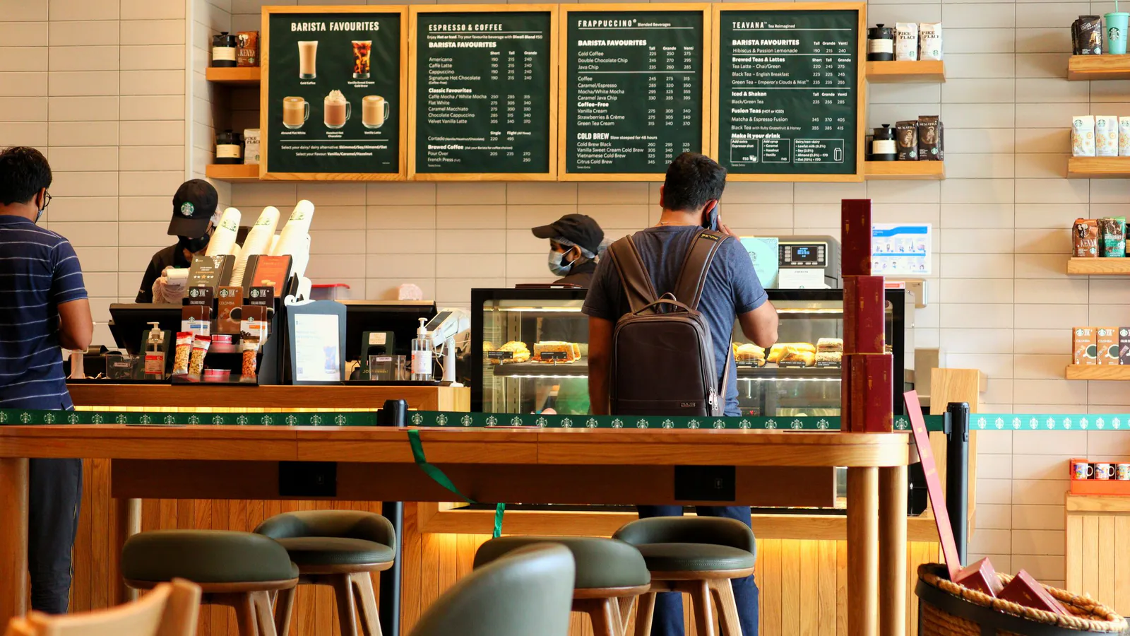 Clientes en la barra de una cafetería moderna pidiendo bebidas y pasteles en ambiente acogedor | ZonaFranquicia