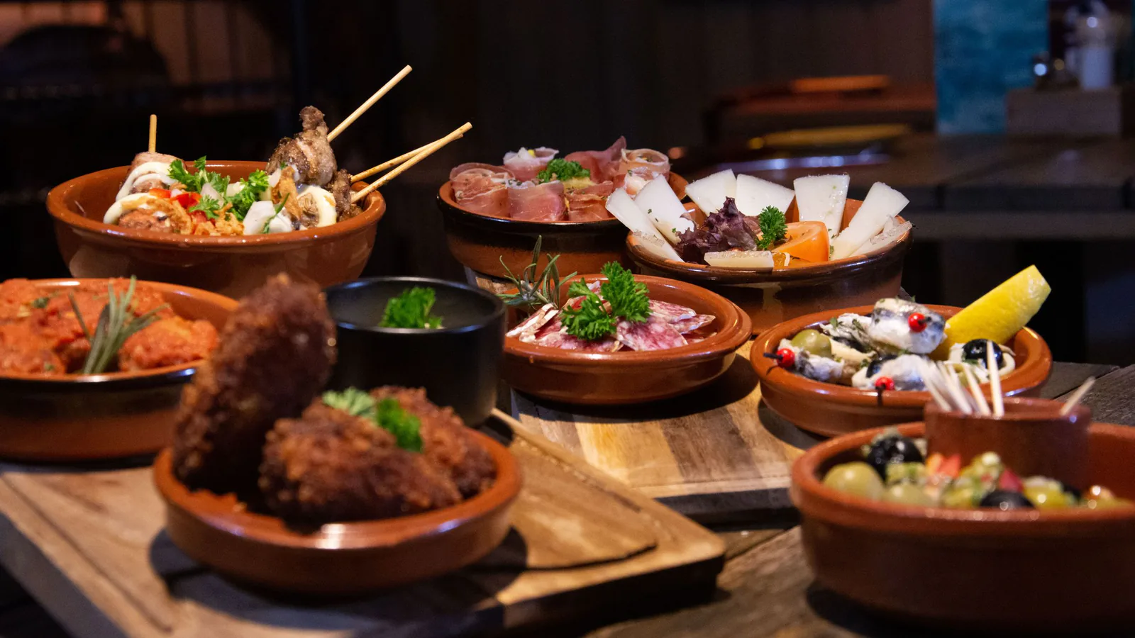 Mesa con variedad de tapas españolas elegantemente presentadas en ambiente acogedor de restaurante tradicional | ZonaFranquicia