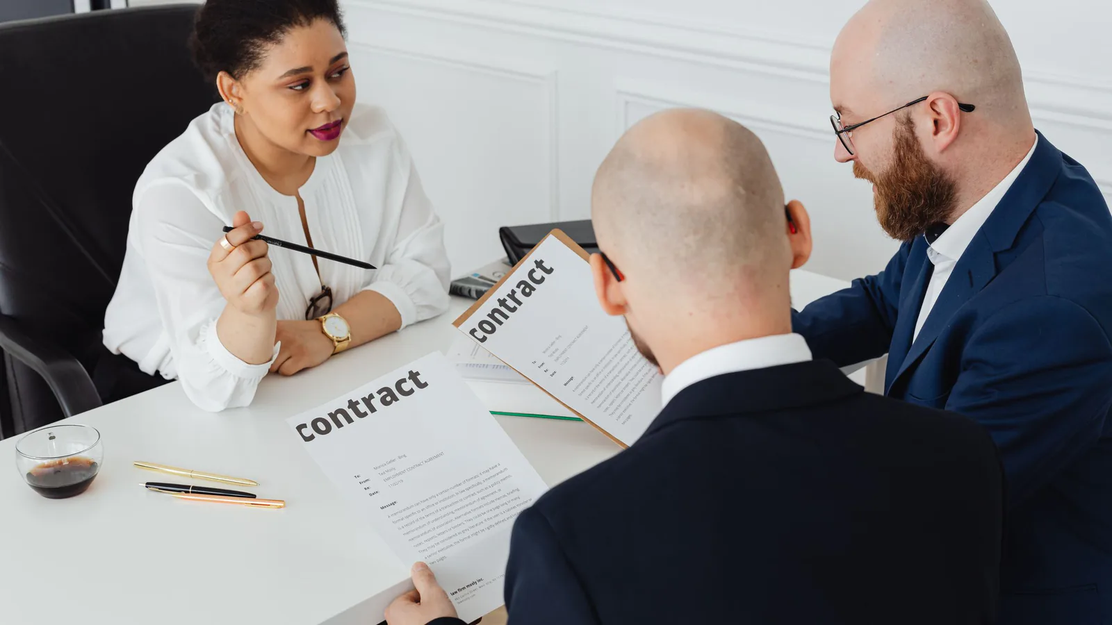 Preguntas clave que debes hacer al franquiciador antes de invertir | ZonaFranquicia Tres profesionales de negocios revisan y discuten un contrato en una oficina moderna. | ZonaFranquicia