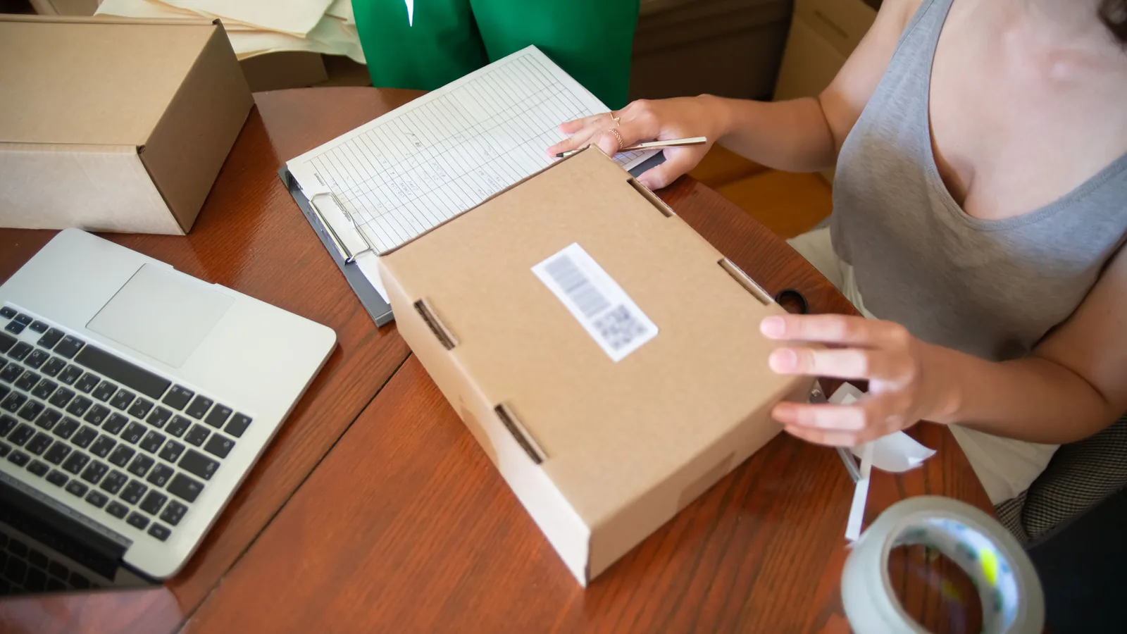 Dos personas empaquetando pedidos en un pequeño negocio con laptop, ilustrando operaciones de e-commerce | ZonaFranquicia