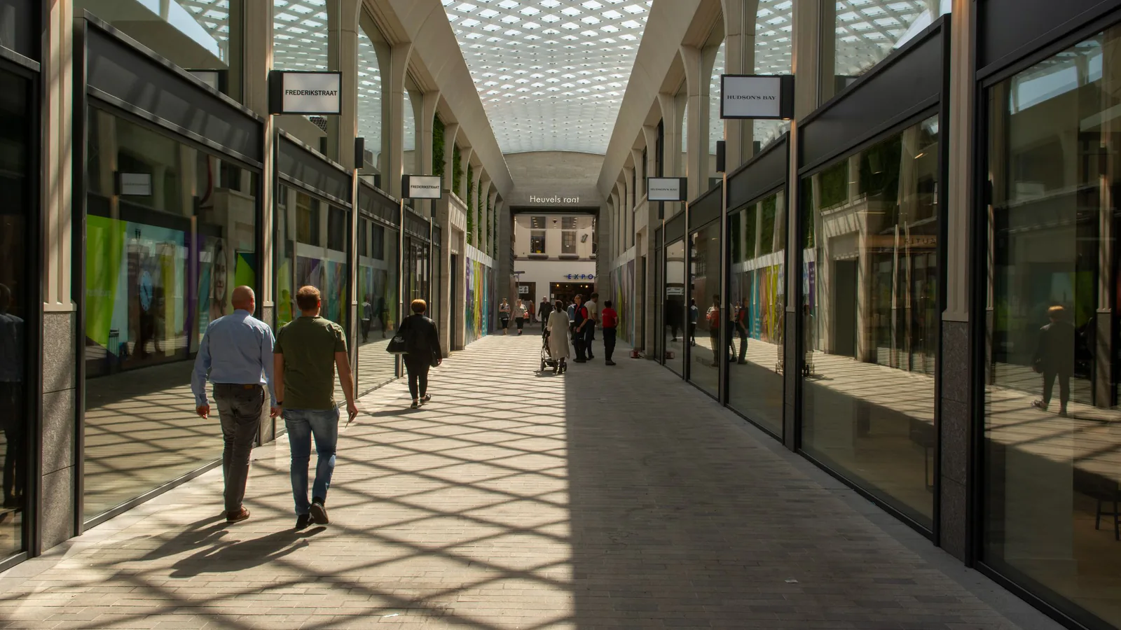 Shopping center vs street retail: cálculo real de viabilidad para tu franquicia | ZonaFranquicia Pasillo moderno de centro comercial con tiendas, clientes caminando bajo techo de cristal | ZonaFranquicia