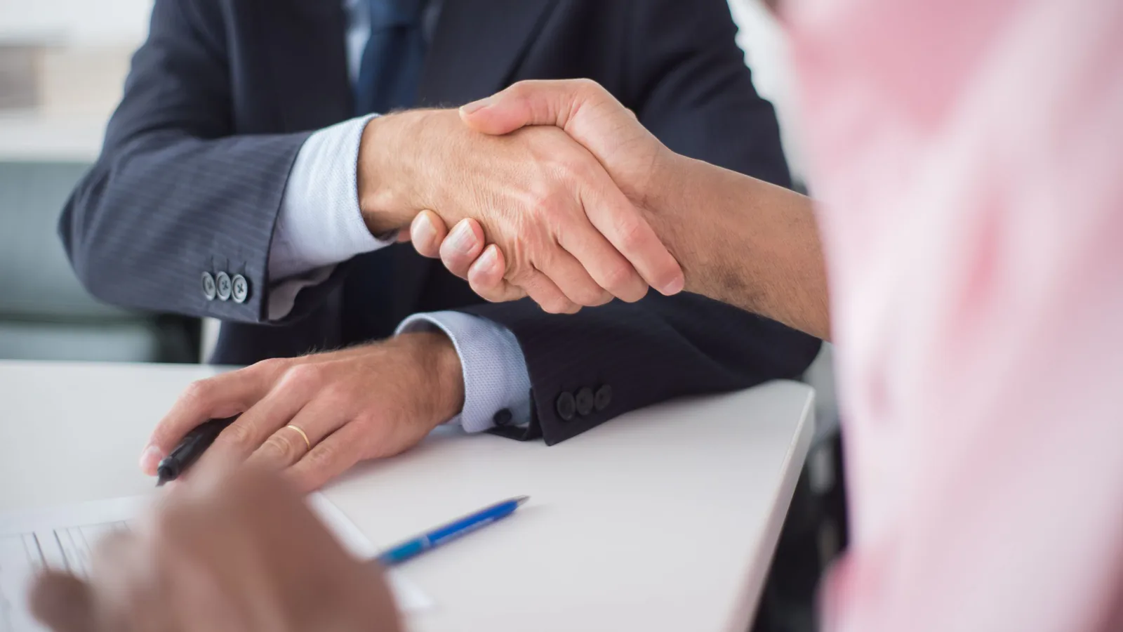 Territorios en franquicia: exclusividad y derechos que debes proteger | ZonaFranquicia Dos empresarios se estrechan la mano sobre la mesa, sellando un acuerdo comercial en oficina | ZonaFranquicia