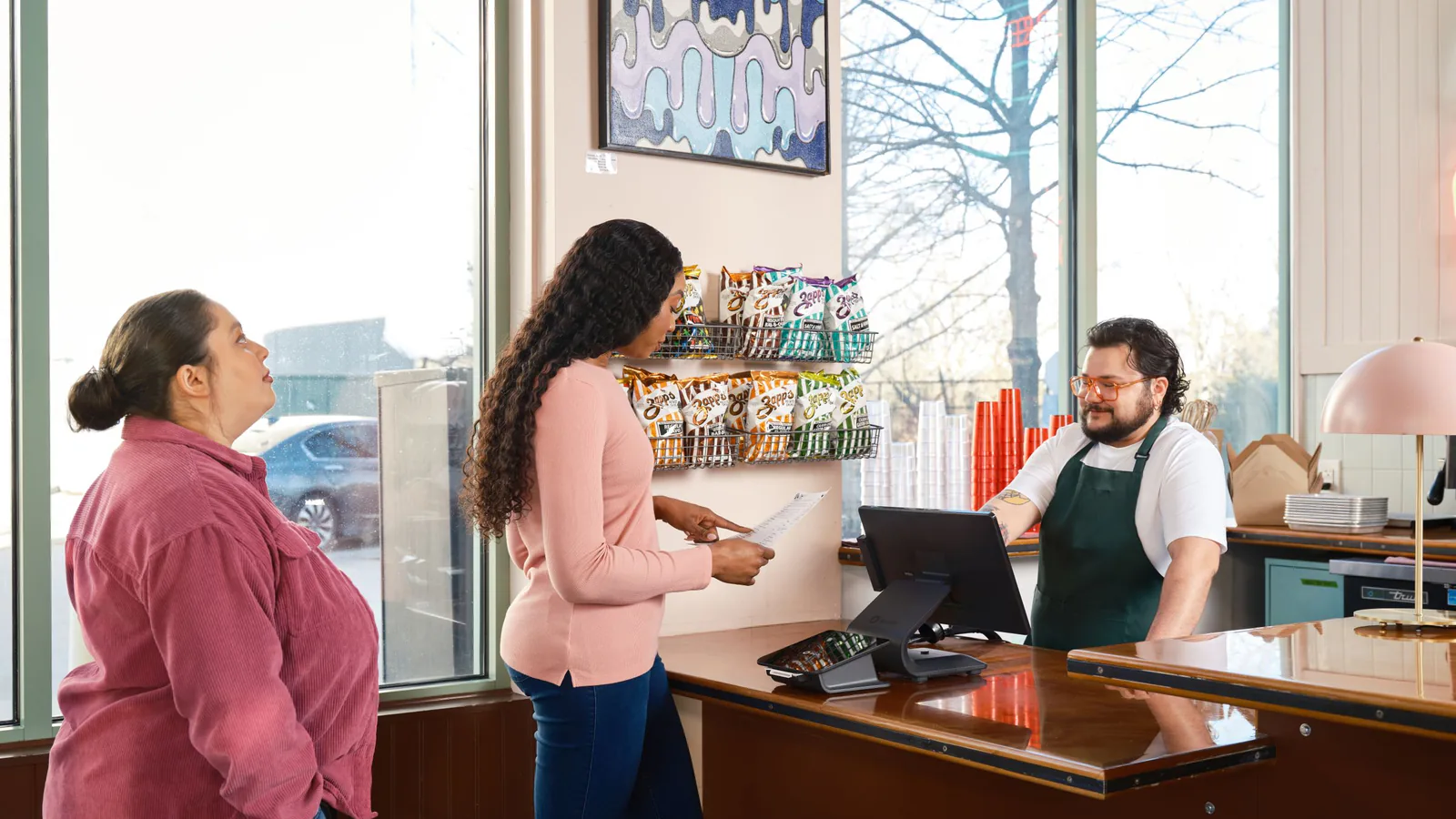 Wingstop abre en Barcelona y acelera su expansión física en España tras años de solo delivery | ZonaFranquicia Dos clientes interactúan con personal en mostrador de punto de venta de restaurante moderno | ZonaFranquicia